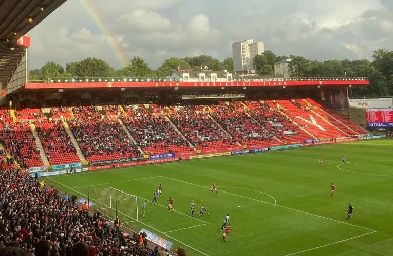 Sân vận động The Valley rực rỡ trong ngày thi đấu, với cờ hoa và đông đảo cổ động viên Charlton Athletic